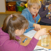 Eine Schülerin und ein Schüler beobachten die Brechung in einem Becherglas voll Wasser.