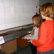 Zwei Schülerinnen leuchten mit Hilfe einen Spiegels den Weg durch ein aufgemaltes Labyrinth.